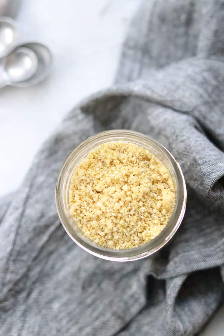 overhead shot of vegan parmesan cheese in small jar with gray napkin and teaspoons nearby