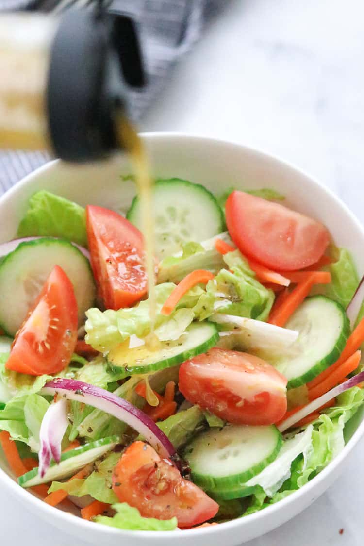 overhead shot of homemade Italian dressing being poured onto cucumber lettuce and tomato salad in a white bowl