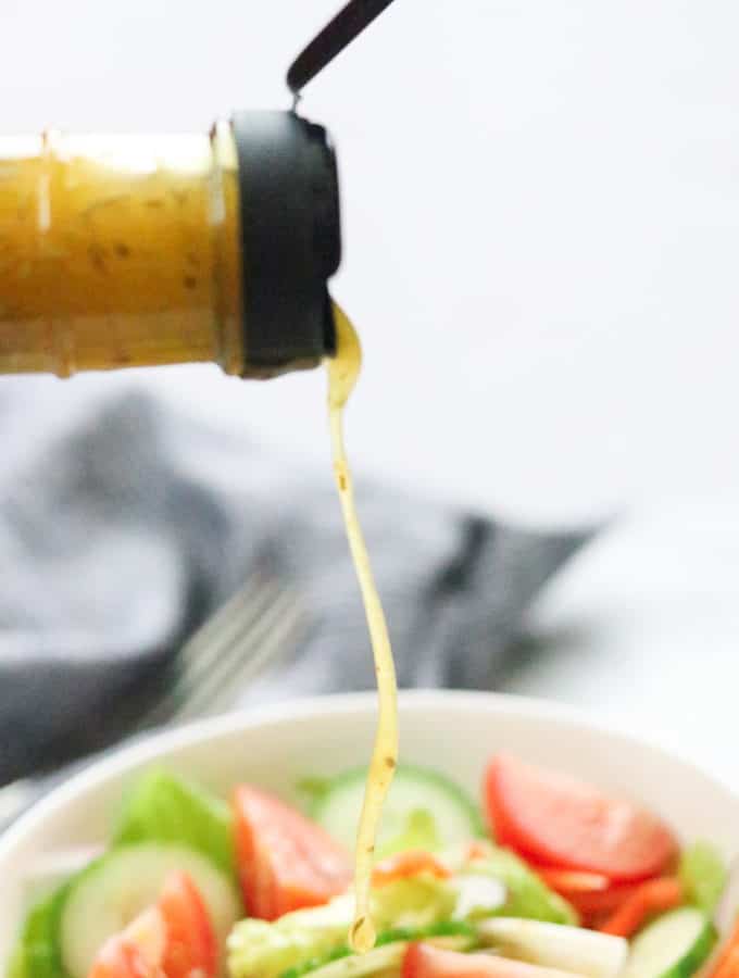side shot of homemade Italian dressing being poured onto bowl of salad with napkin in background