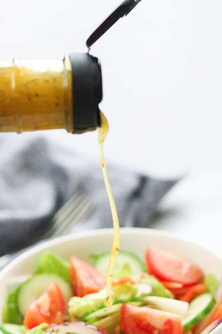 side shot of homemade Italian dressing being poured onto bowl of salad with napkin in background