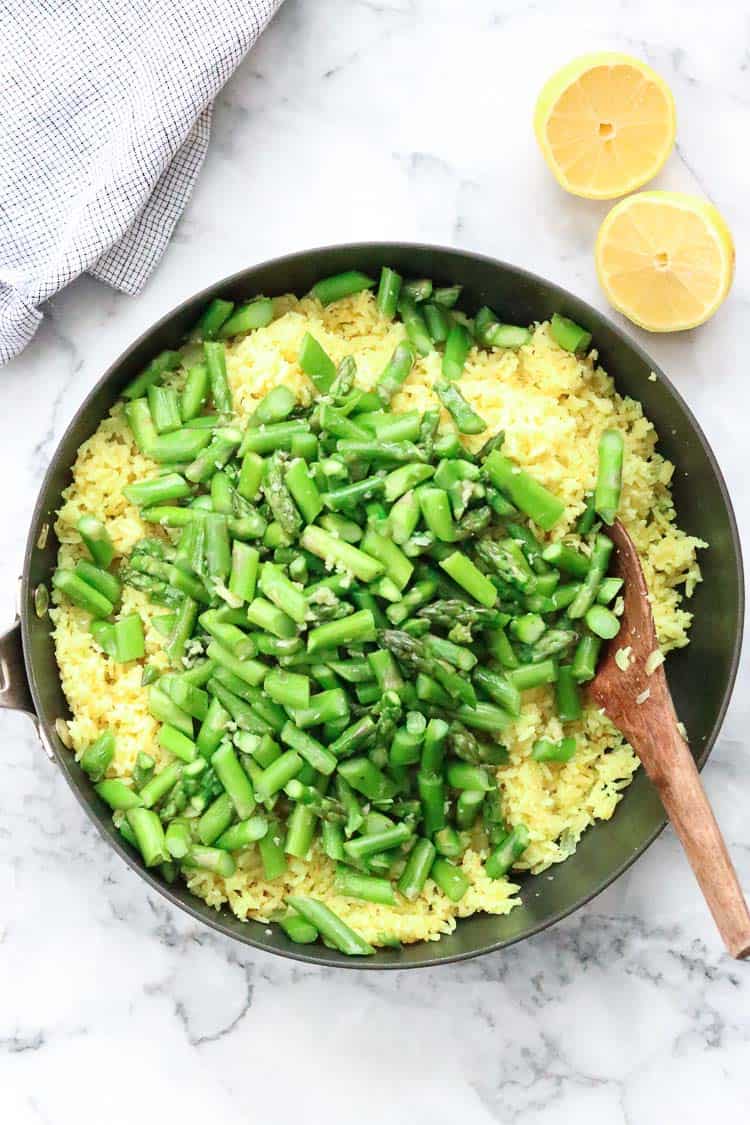 lemon rice in large black skillet topped with sautéed asparagus and lemon halves beside 