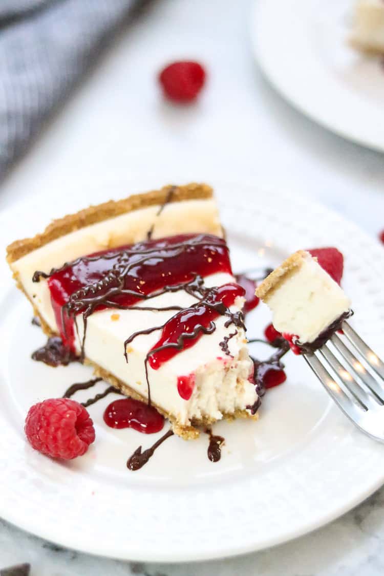 side overhead shot of vegan cheesecake with various drizzles and fresh raspberries with a fork bite taken off the end and resting nearby