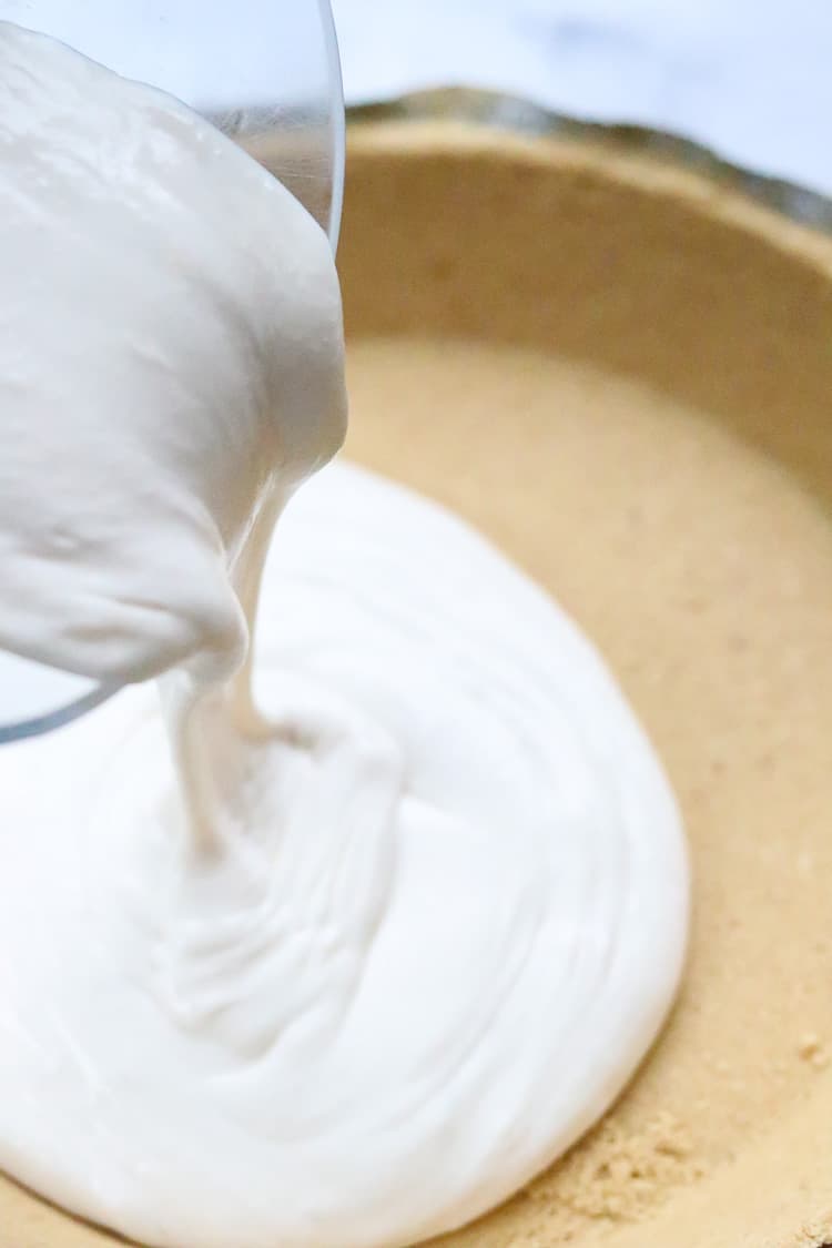 pouring vegan cheesecake mixture into graham cracker pie crust