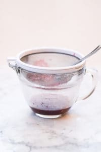straining raspberry seeds through a sieve into a cup