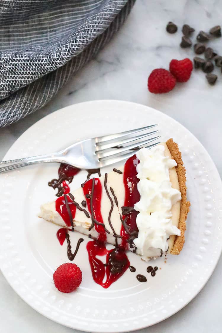 vegan cheesecake with fork beside on a white plate drizzled with raspberry sauce