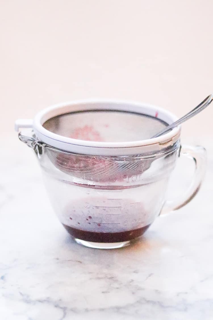 frozen raspberry juice being expressed through a sieve for topping vegan cheesecake