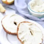 side overhead shot of two halves of a bagel spread with vegan cream cheese on a white plate