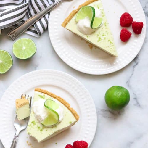 overhead shot of two slices of vegan key lime pie on white plates with fresh raspberries beside