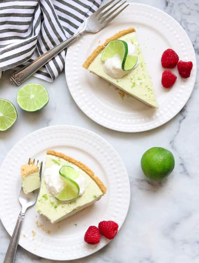 overhead shot of two slices of vegan key lime pie on white plates with fresh raspberries beside