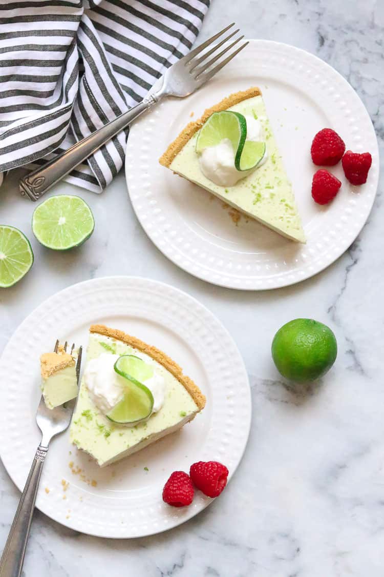 overhead shot of vegan key lime pie on two plates with slice limes and whip cream for garnish