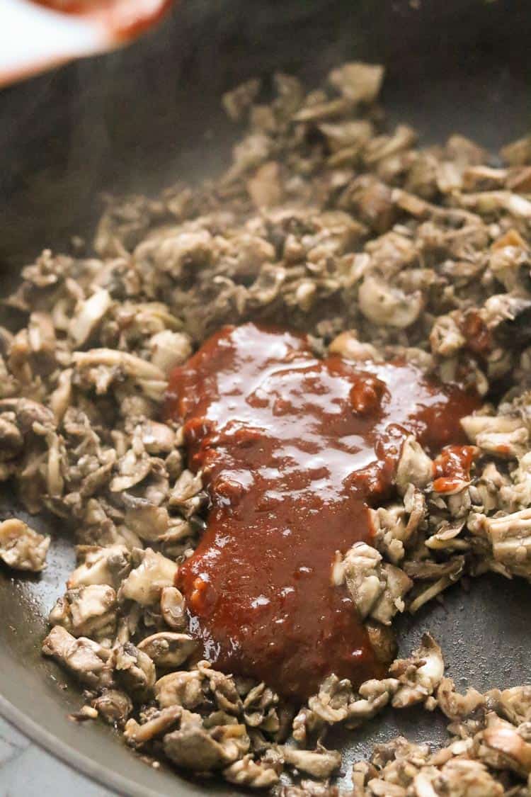 overhead shot of cooked mushrooms in skillet with barbecue sauce being added