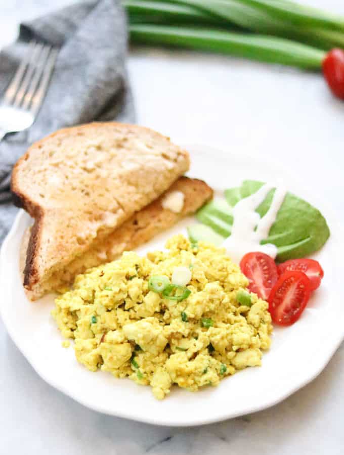side overhead shot of tofu scramble on a white plate with toast, avocado and sliced tomatoes