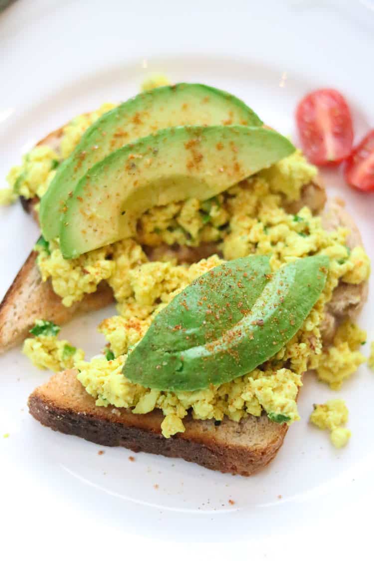 side overhead closeup shot of toast topped with tofu scramble and avocado slices garnished with cayenne pepper