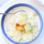 overhead shot of vegan corn chowder in a bright blue bowl on a white plate topped with croutons