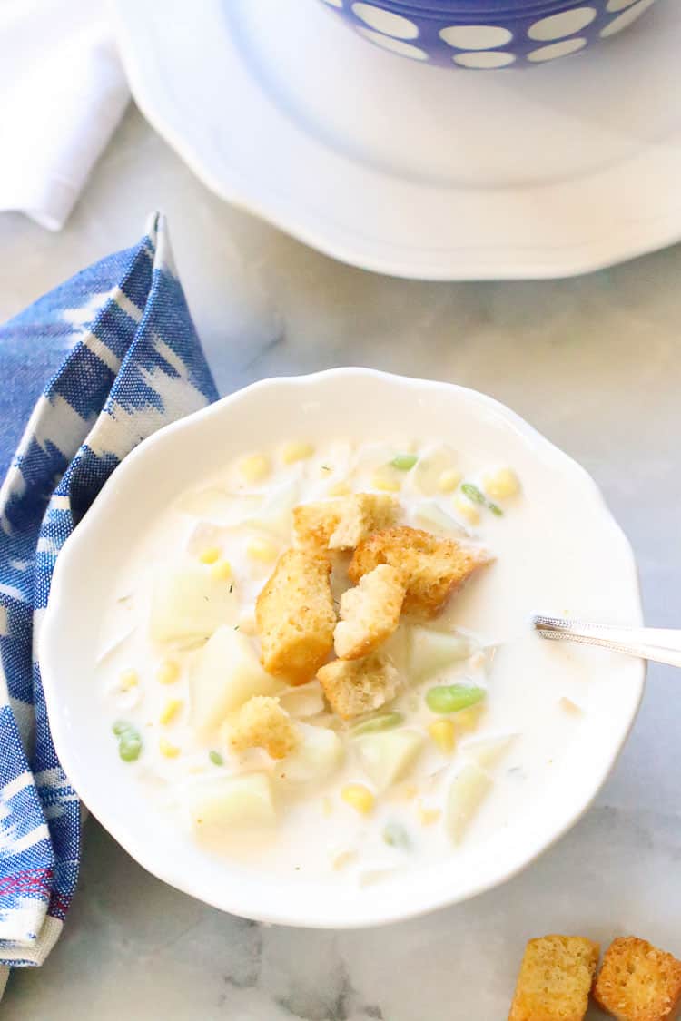 overhead shot of vegan corn chowder soup in white bowl with croutons and blue and white napkin