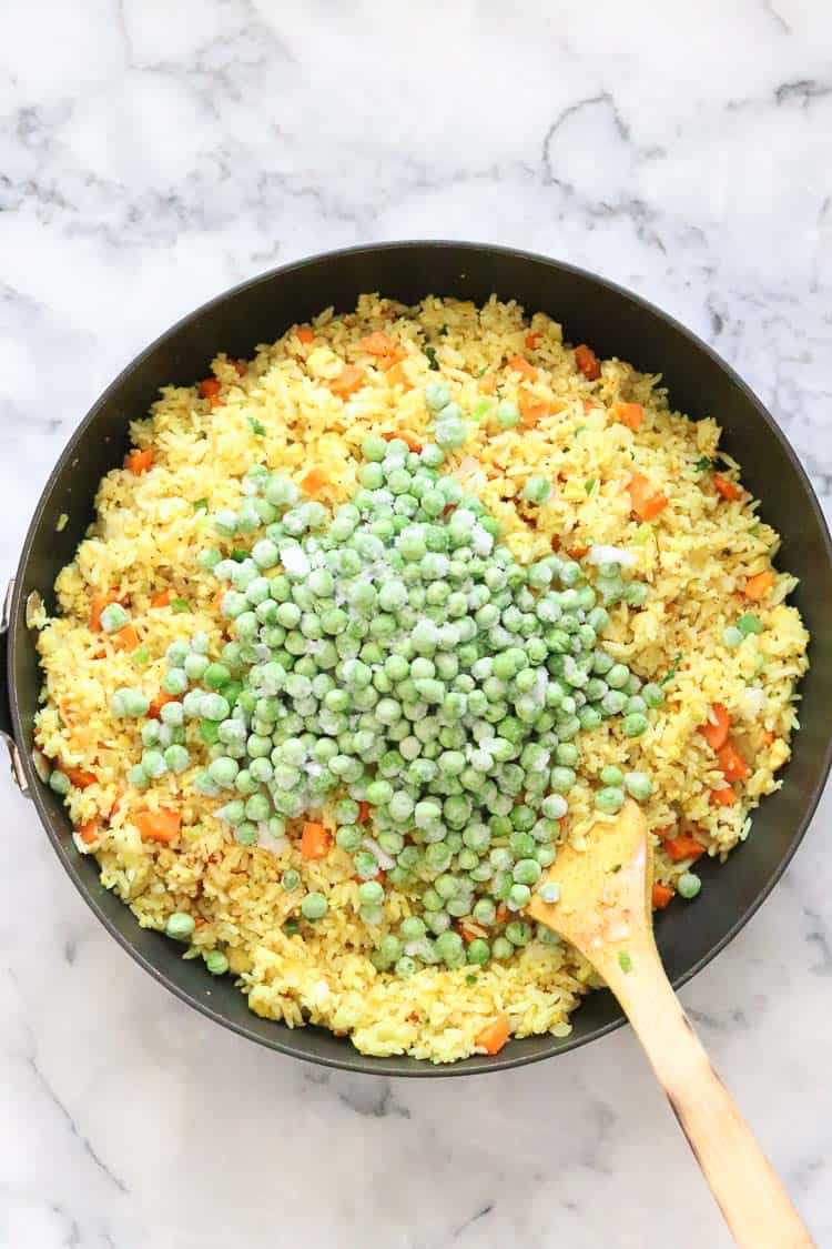 overhead shot of frozen green peas added to skillet of vegan fried rice