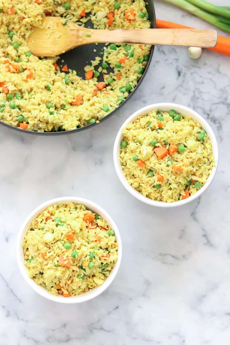 overhead shot of vegan fried rice being served from black skillet into two white bowls on marble background