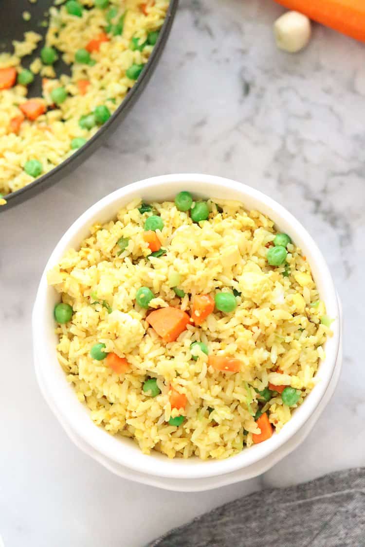 overhead shot of vegan fried rice with diced carrot and peas in a white double bowl 