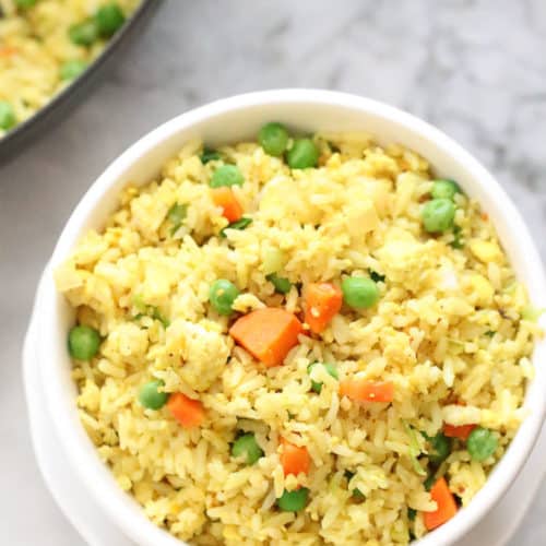 overhead closeup shot of vegan fried rice in white double bowl with skillet in background and wooden spoon