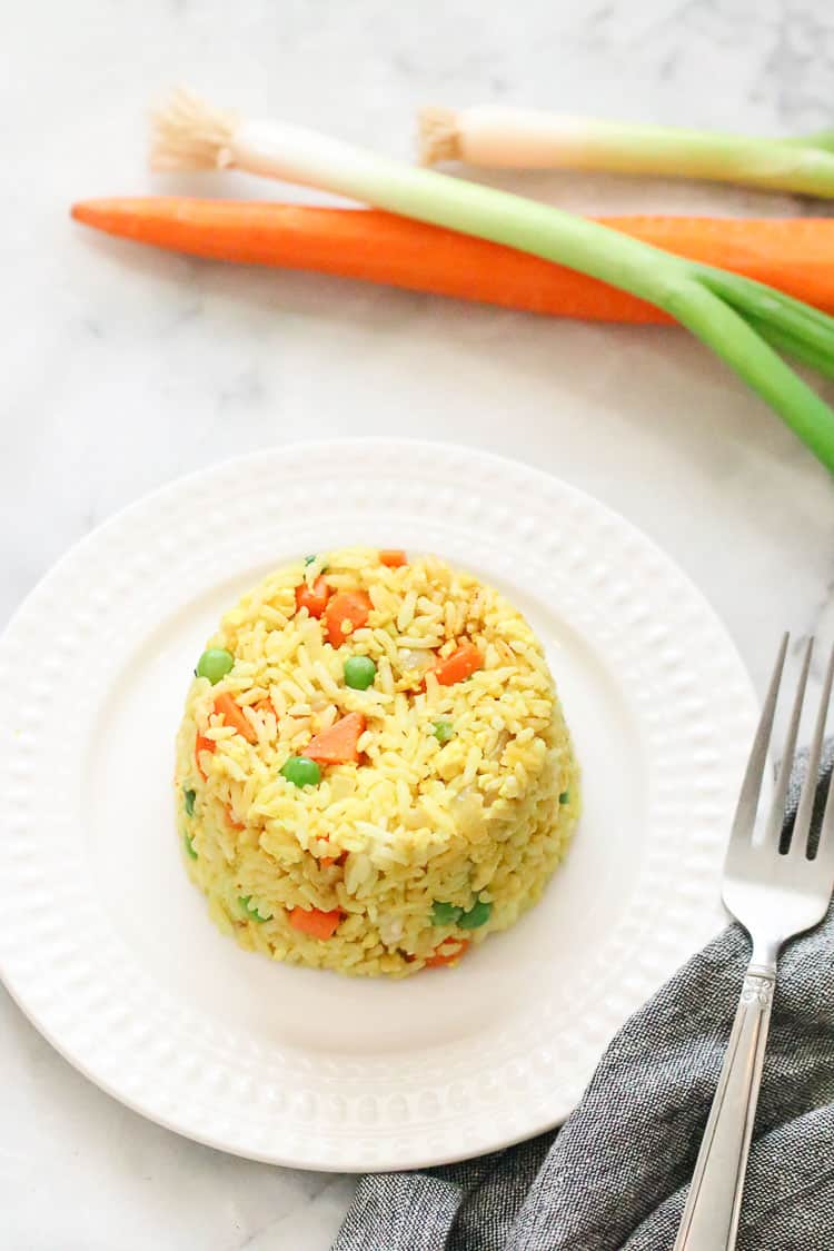 overhead shot of vegan fried rice in a round shape on a white plate with peeled carrot and green onion nearby