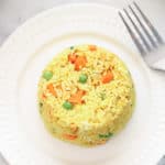overhead shot of vegan fried rice in a round shape on a white plate with carrots and peas