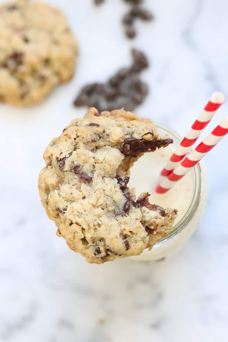 overhead closeup shot of vegan chocolate chip cookie with a bite taken out resting on top of a mason jar glass of non-dairy milk