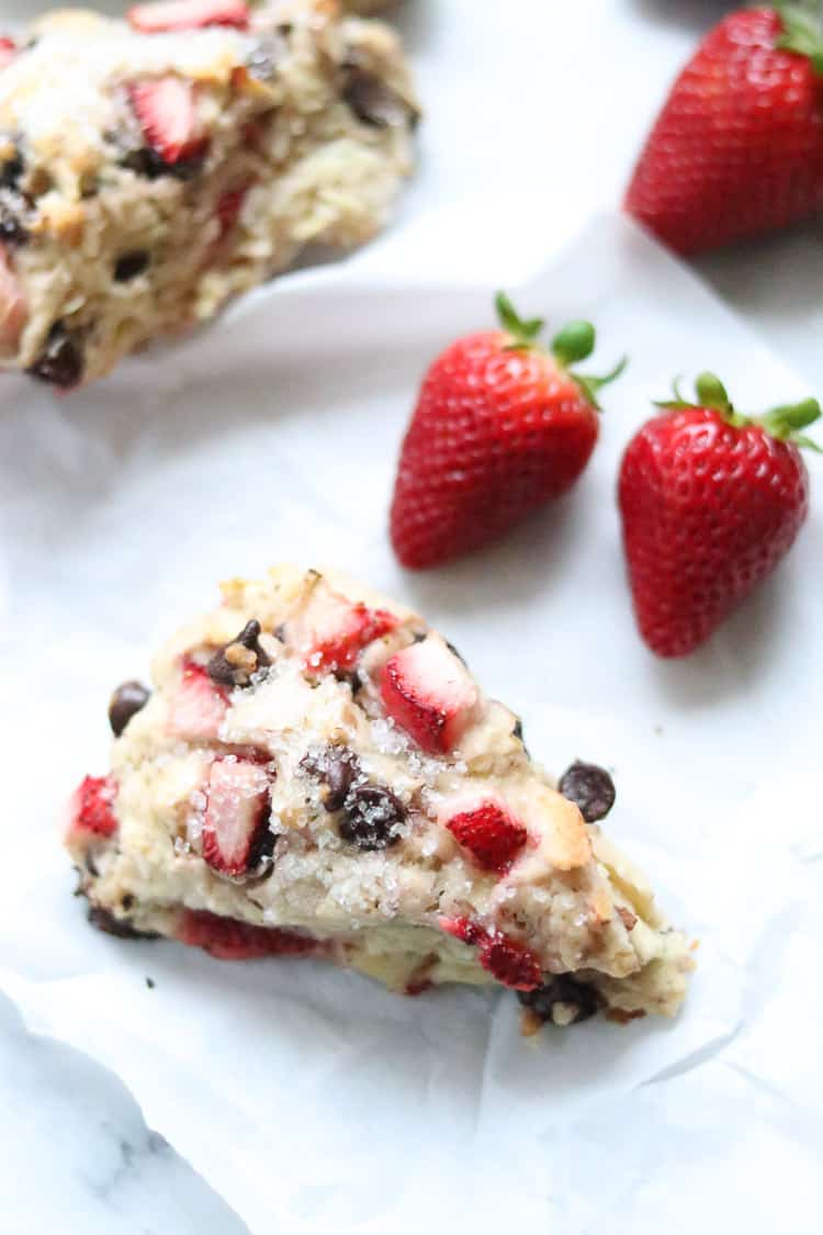 overhead closeup shot of vegan scone on parchment paper with whole fresh strawberries beside