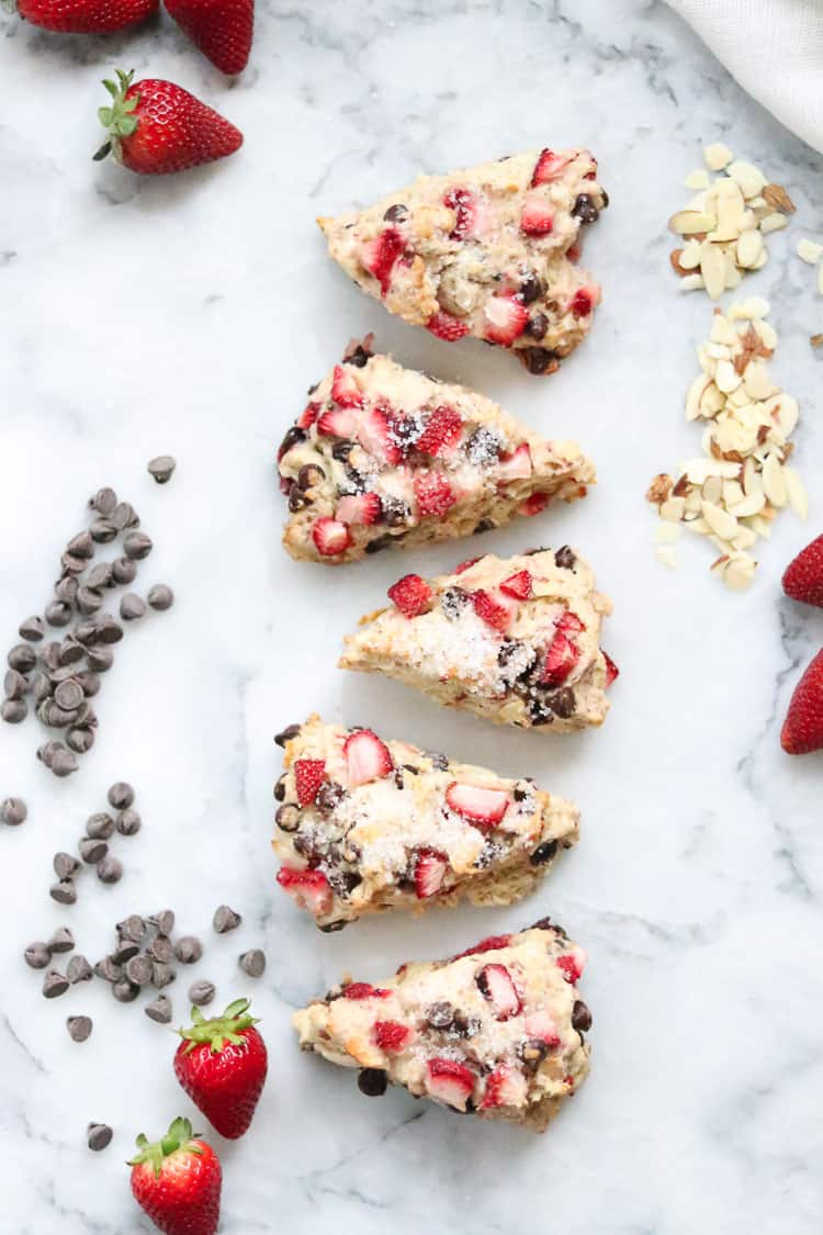 wide overhead shot of 5 vegan scones lined up with chocolate chips and fresh strawberries beside