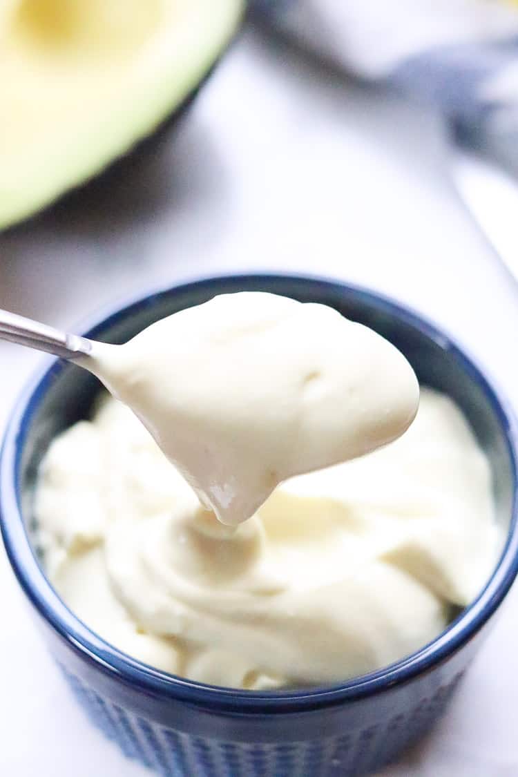 overhead shot of vegan mayo being lifted on a silver spoon above blue ramekin 
