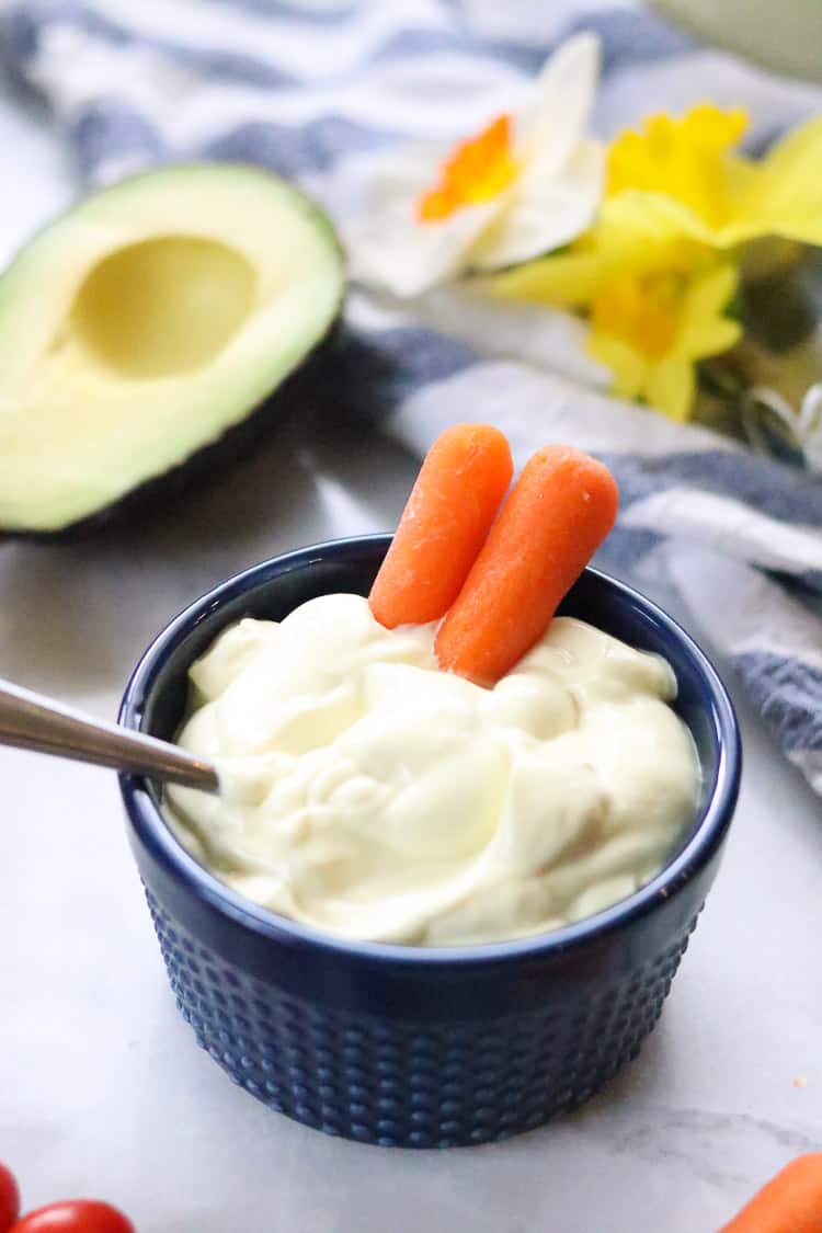 side overhead shot of vegan mayo in blue ramekin with two carrot sticks in it