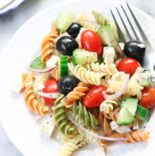 overhead closeup shot of vegan pasta salad on a white plate with a fork