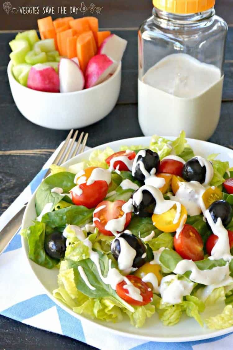 side overhead shot of green salad with vegan ranch dressing drizzled over tomatoes and olives