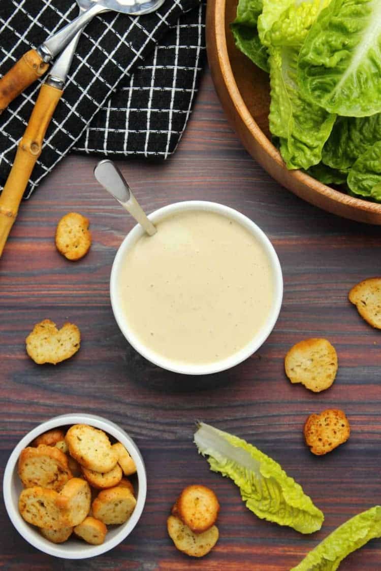 overhead shot vegan caesar salad dressing in a white bowl with croutons and lettuce nearby