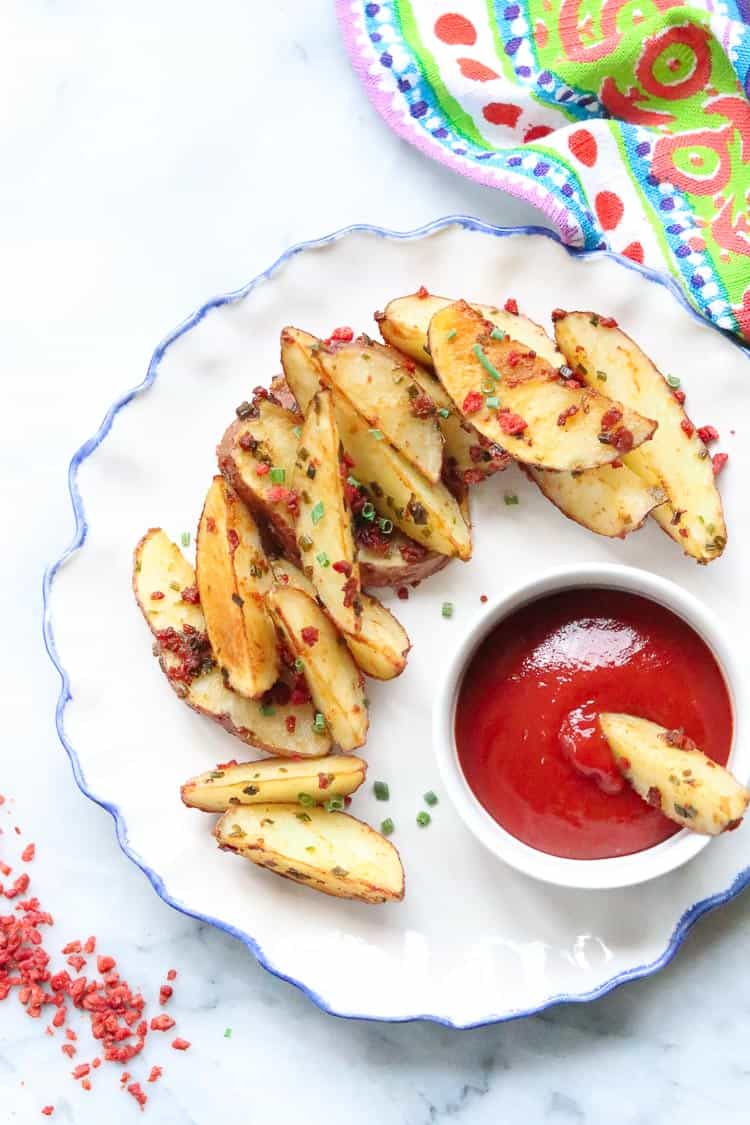 overhead shot of baked potato wedges on a white plate with blue trim and ramekin of ketchup