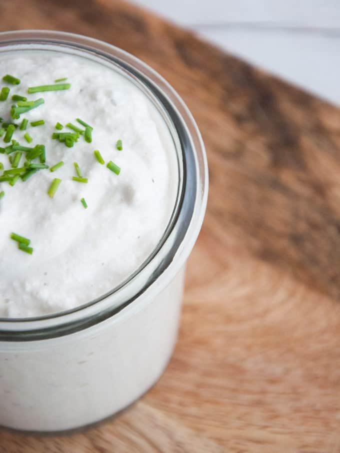 overhead closeup shot of vegan salad dressing in a clear tall container with fresh chopped chives on top