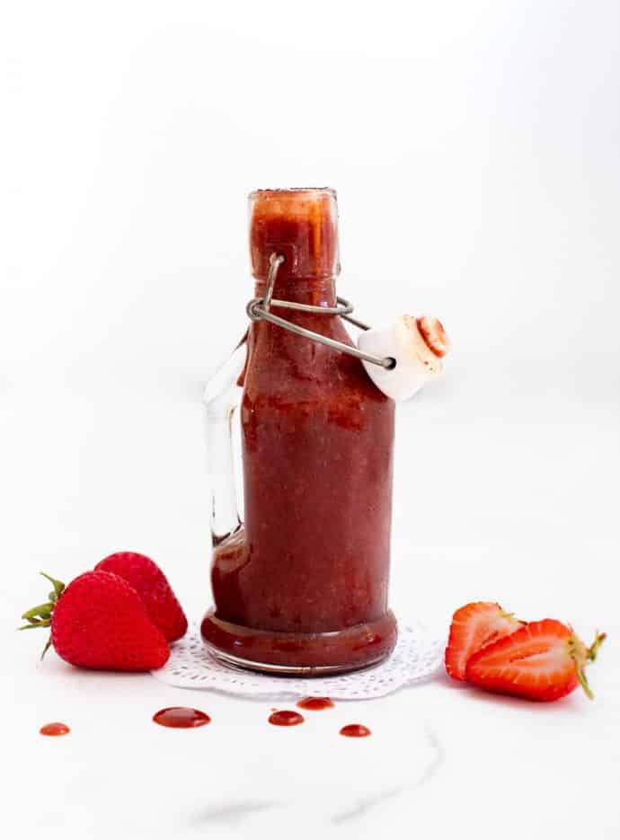 side shot of strawberry vinaigrette dressing in a clear pitcher with strawberries nearby
