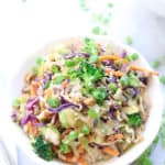 overhead shot of vegan stir fry piled high in a white bowl garnished with chopped green onions and sesame