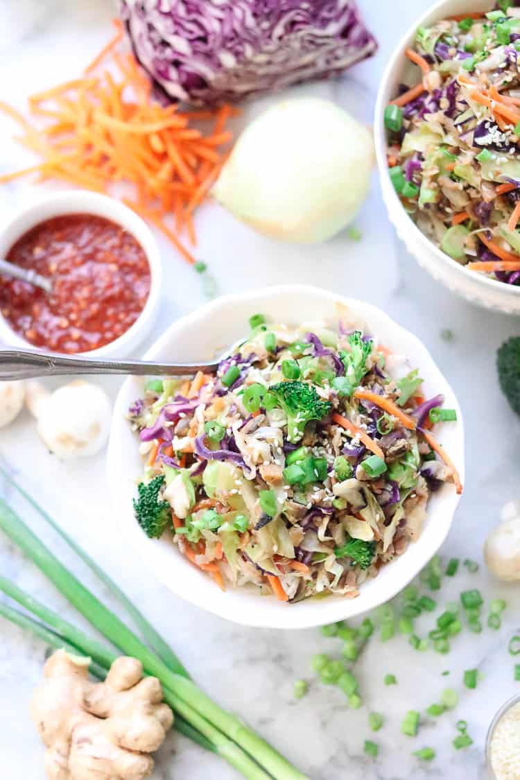 wide overhead shot of vegan egg roll in a white bowl with veggie contents scattered all around on a marble background