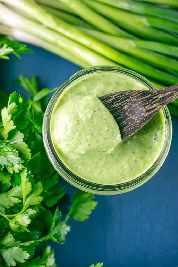 overhead shot of green vegan salad dressing in a jar with some on a wooden spoon and cilantro and green onions nearby