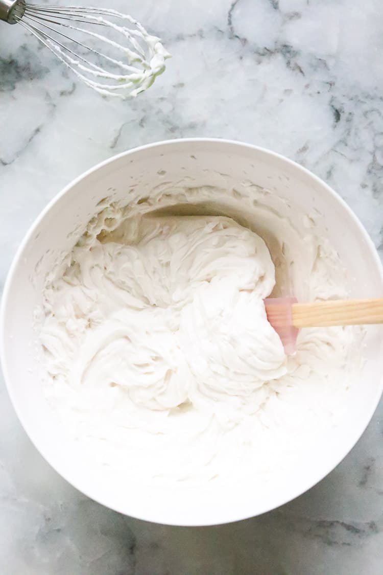 overhead shot of completed vegan whip cream in a bowl with spatula and beater beside