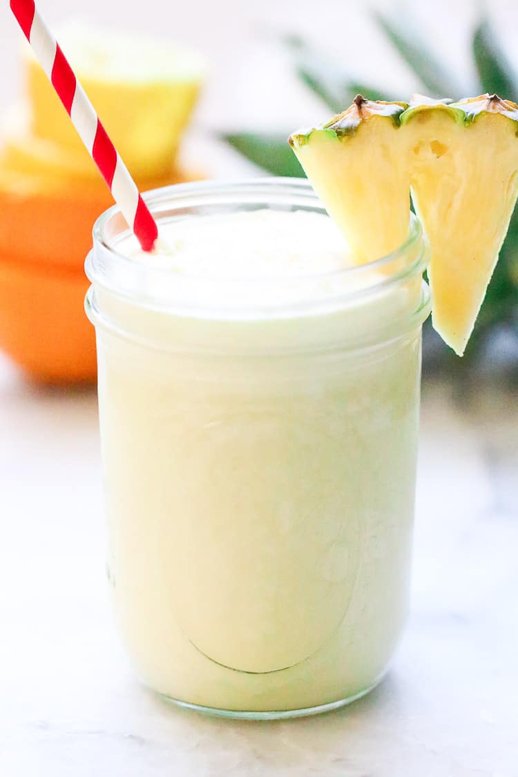 side shot of virgin pina colada smoothie in a pint jar with striped straw and pineapple slice on the side