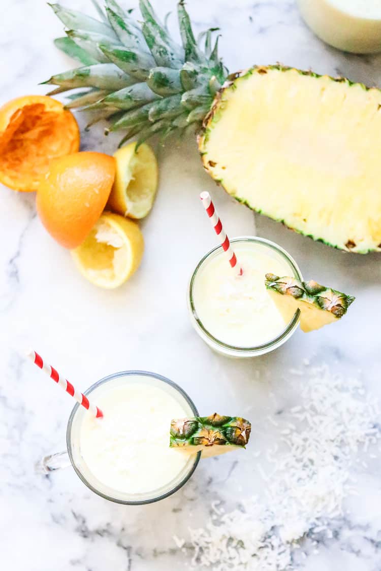 overhead shot of virgin pina colada in a glass and jar with pineapple half and rinds from orange and lemon 