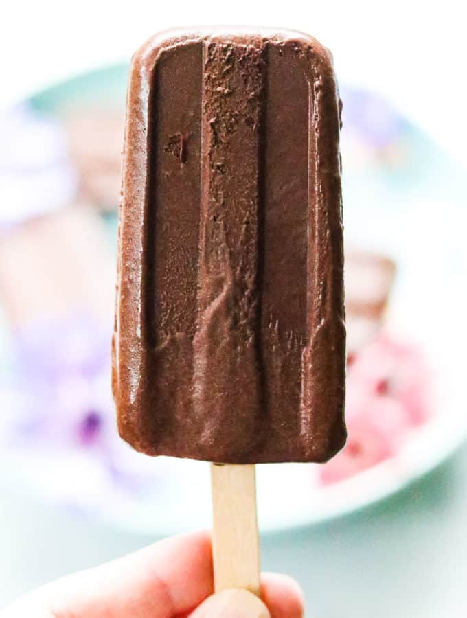 side closeup shot of a vegan fudgesicle on a wooden stick being held upright