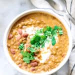 overhead photo of madras lentils in a white bowl with garnish of cilantro and cilantro