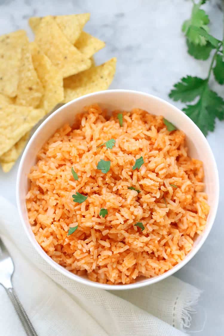 overhead photo of vegan mexican rice in a white serving bowl with fork beside and corn chips in the background