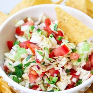 overhead closeup shot of cabbage salsa in a white bowl with a tortilla chip in it