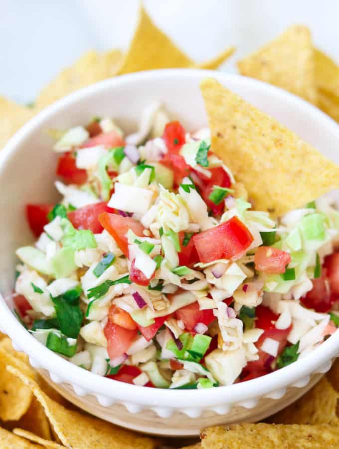 overhead closeup shot of cabbage salsa in a white bowl with a tortilla chip in it