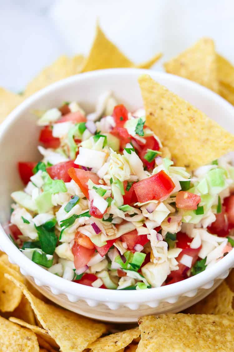 side overhead closeup shot of cabbage salsa in a white bowl surrounded by tortilla chips