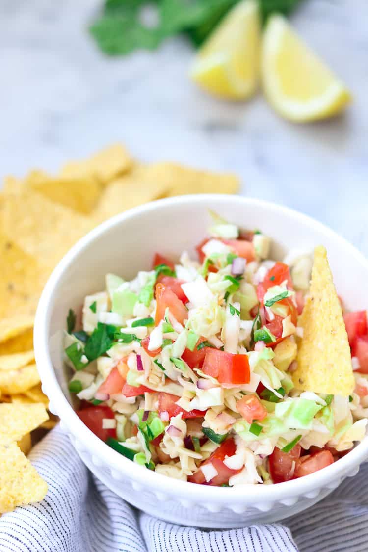 side overhead shot of cabbage pico de gallo salsa on a striped napkin with chips and lemon nearby