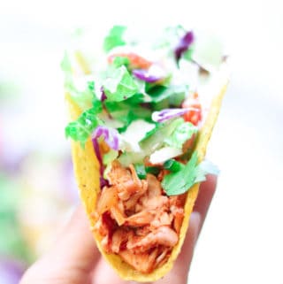 side shot of hand holding vegan jackfruit taco with lettuce and cabbage on top